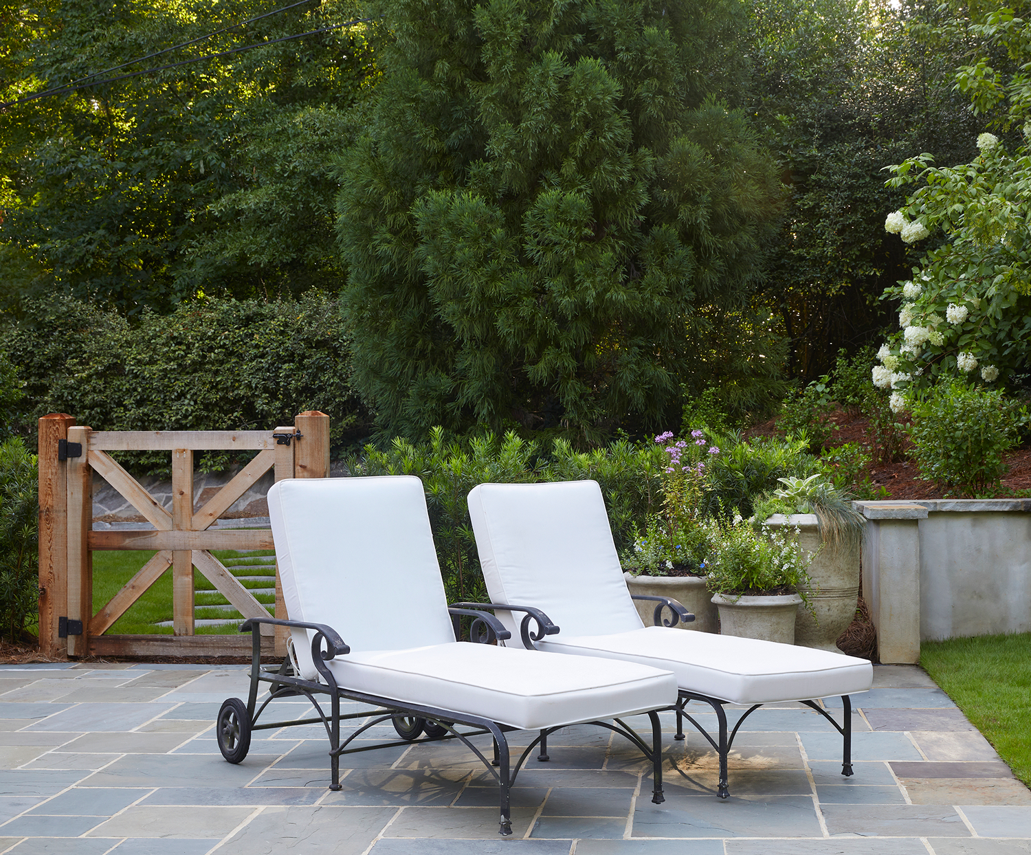 Upscale backyard living area featuring a bluestone terrace, designer lounge chairs, and a custom wooden gate.