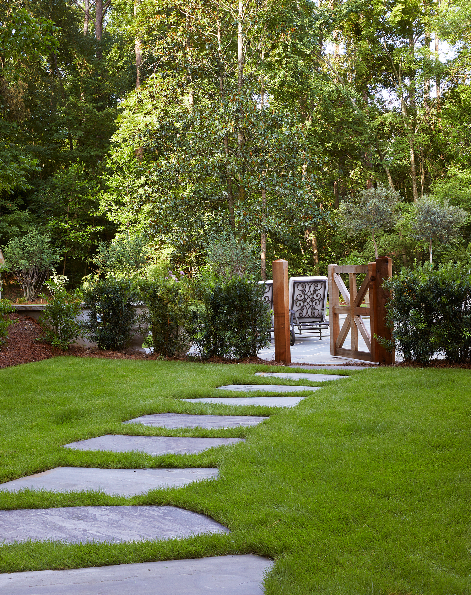 Grey flagstone slab walkway cutting through a lush green backyard lawn toward a hidden pool destination.