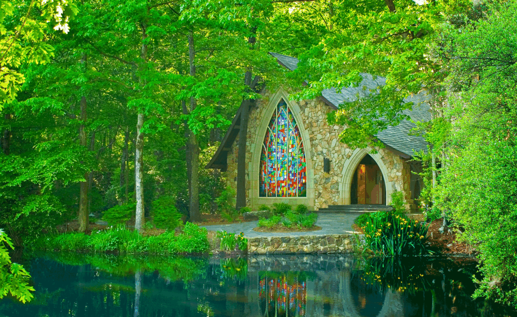 The stone Ida Cason Callaway Memorial Chapel with colorful stained glass windows reflecting in the water.
