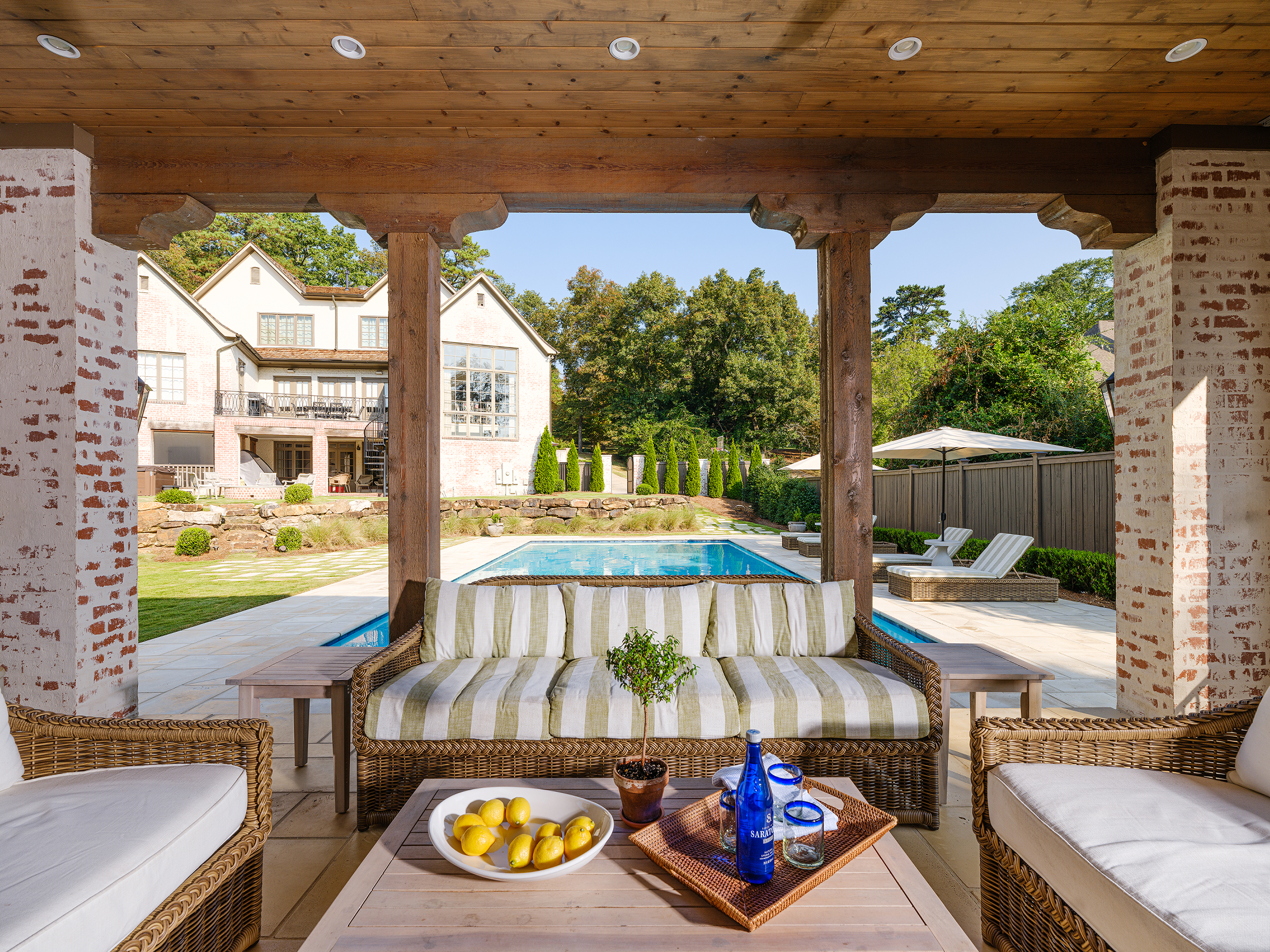 Covered outdoor lounge area with seating and a fireplace at the Mountain Brook pool house, overlooking the pool deck.