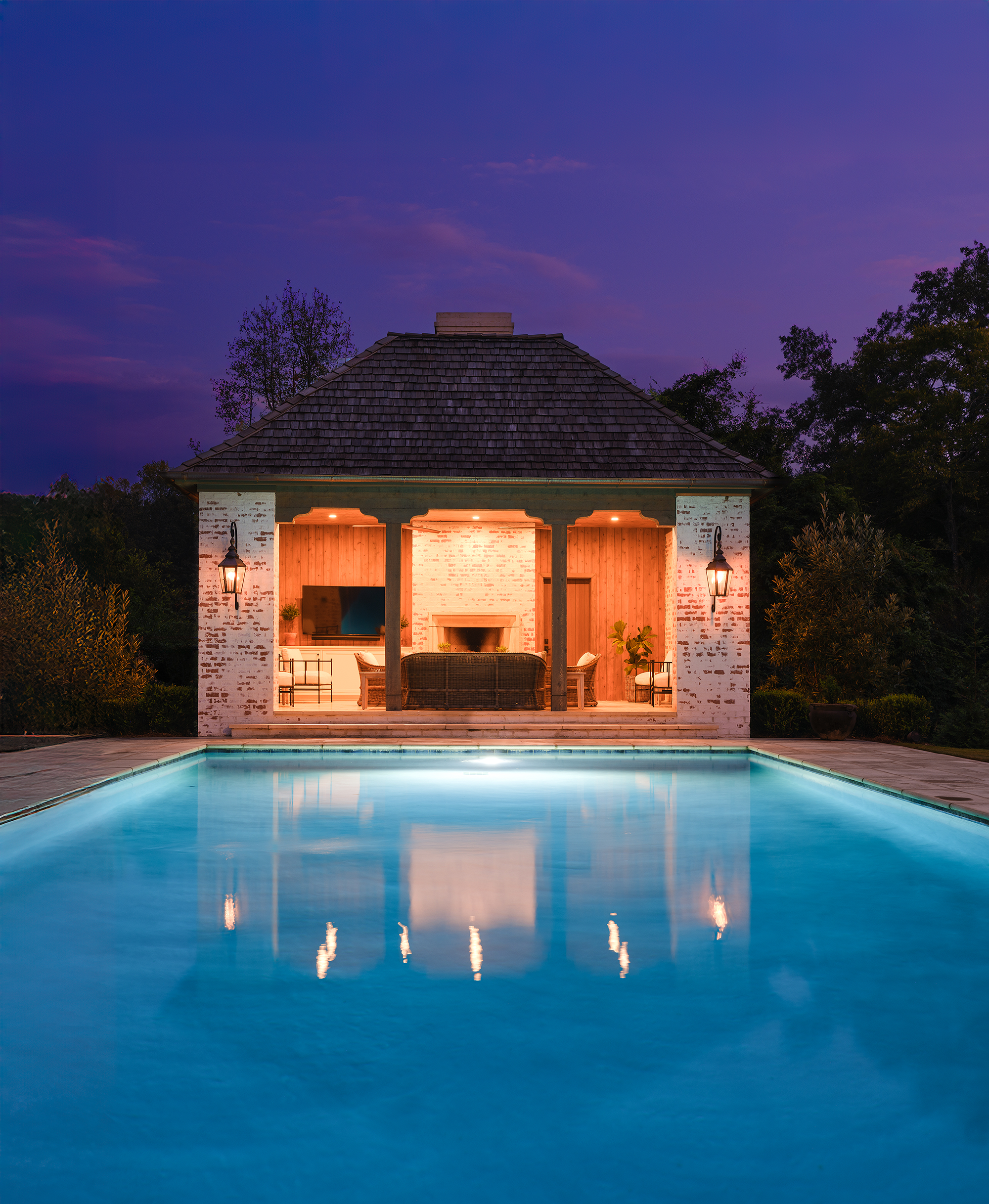 Illuminated swimming pool and pool house at night in Mountain Brook, Alabama, with dramatic landscape lighting.