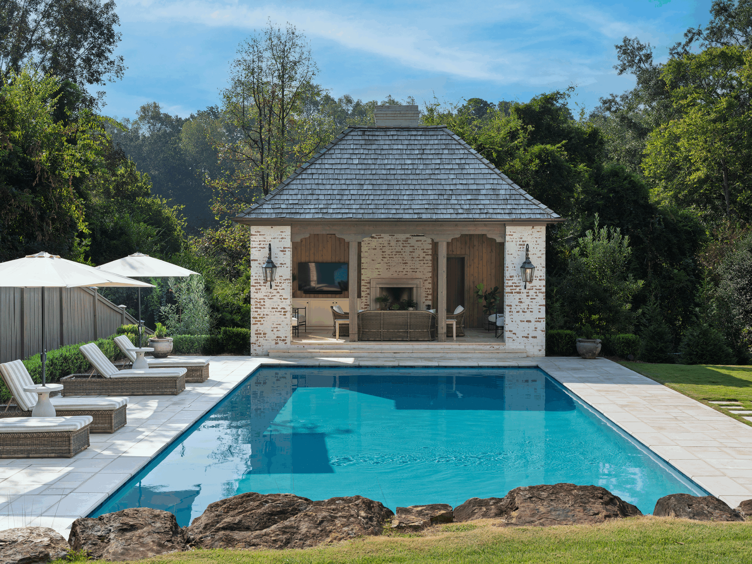 Exterior of a brick pool house with a cedar shake roof beside a swimming pool in Mountain Brook, Alabama, designed by architect David Blackmon.