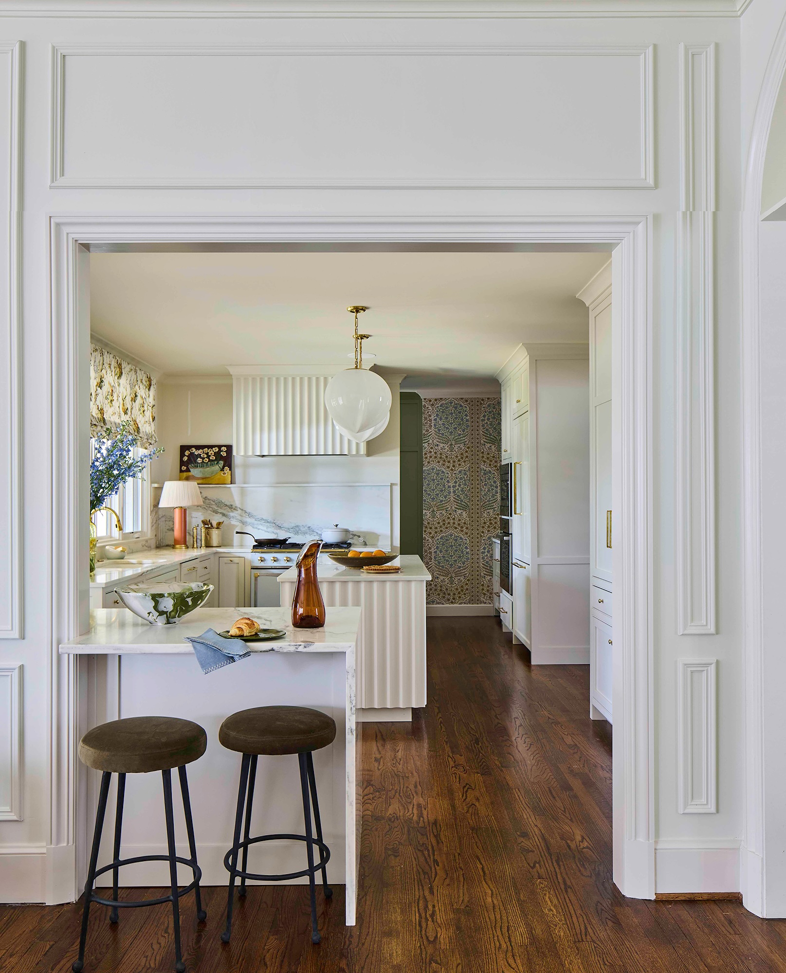 White kitchen with fluted island, custom Alabaster cabinetry by Burnham's Fine Cabinetry, and oversized milk-glass pendant lights in a Mountain Brook, Alabama home designed by Kelly Neely.