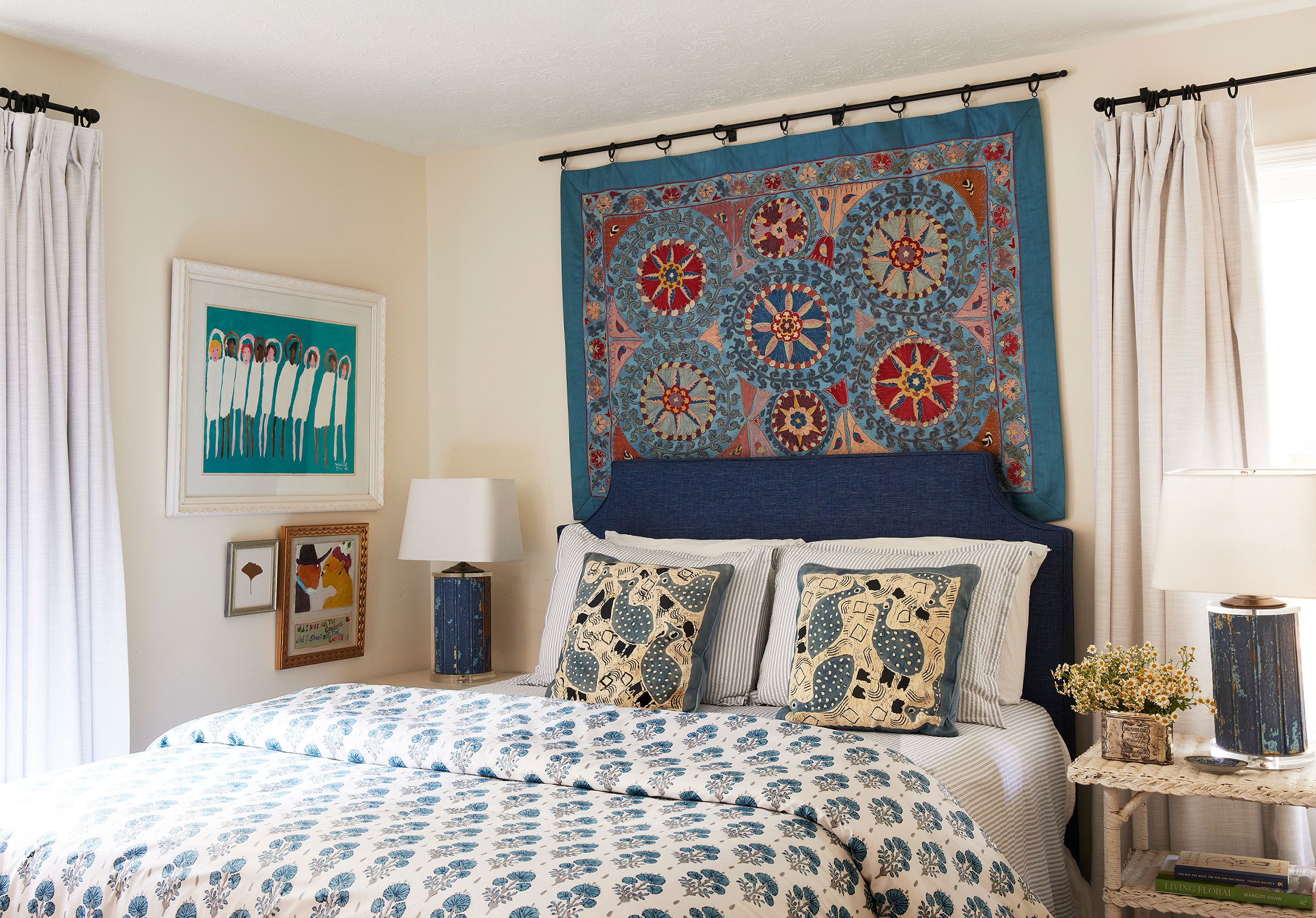 Bed with a vibrant Suzani textile hanging above the headboard, styled with graphic black-and-white bird-print pillow shams at Lake Martin home. 