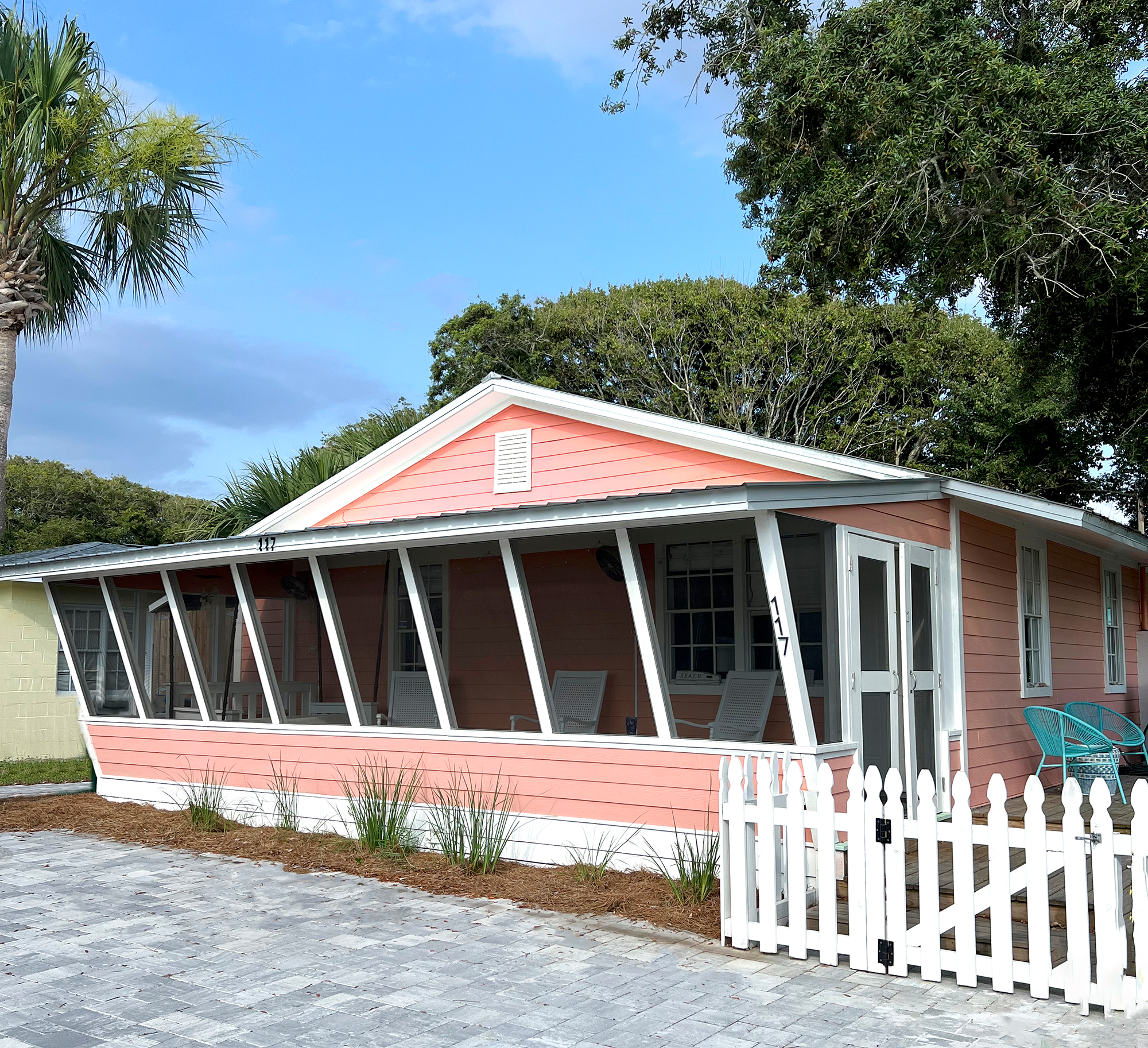 Vibrant coral exterior of a 1940s Panama City Beach cottage with a screened front porch and swinging daybed.