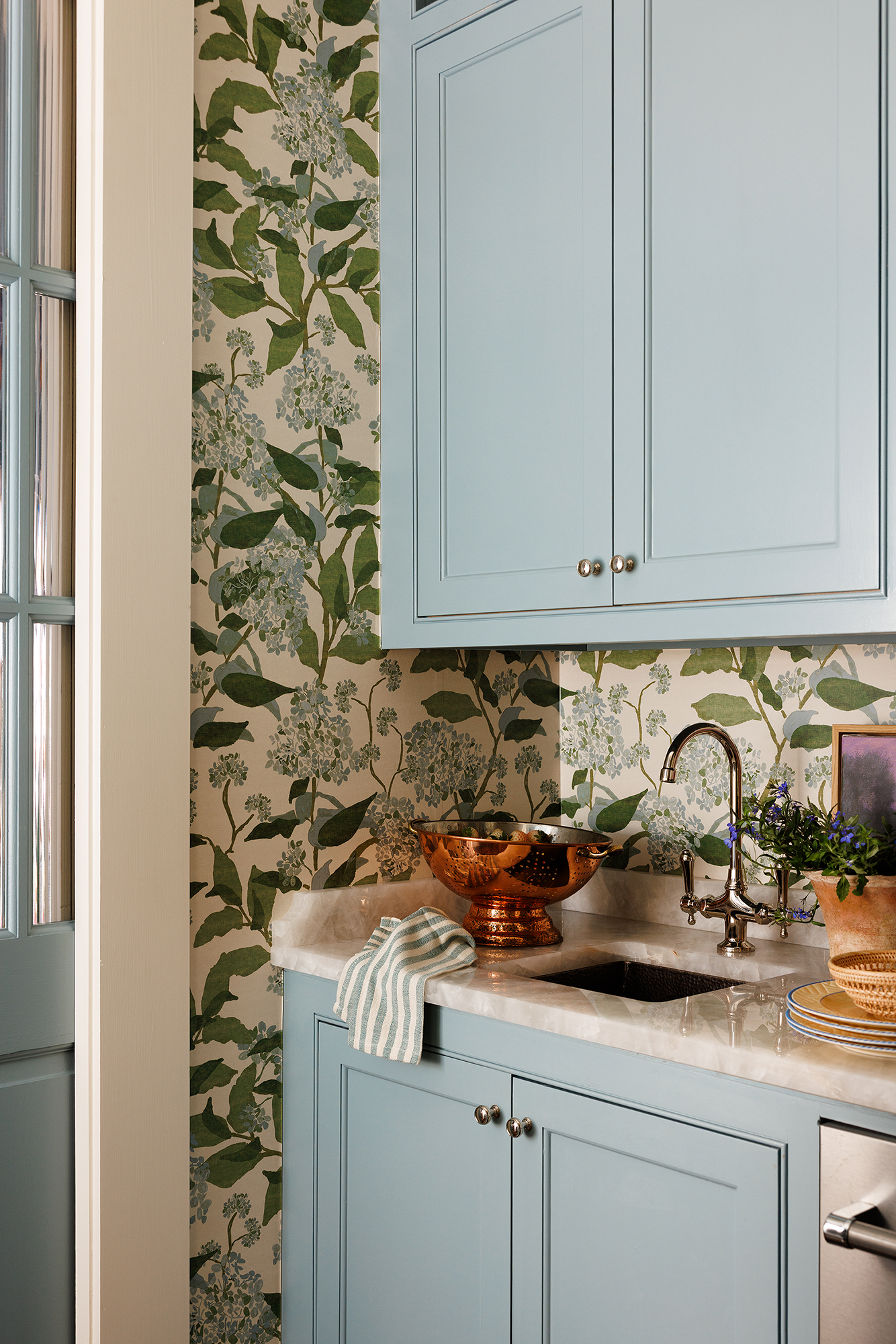 Pantry sink detail with blue cabinetry, floral wallpaper, and copper colander.