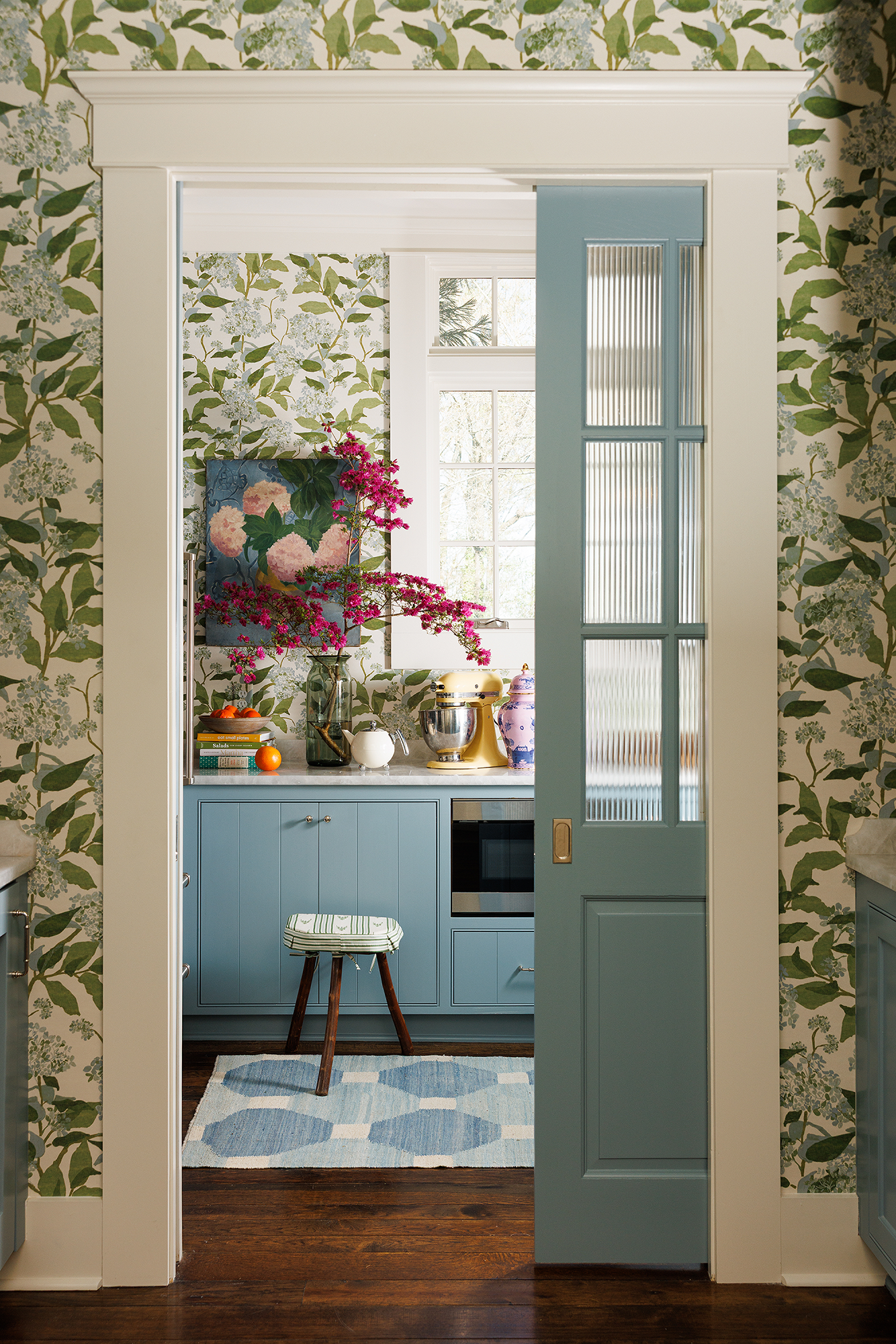 Blue pocket door opening into a wallpapered pantry and bar area of a Mountain Brook kitchen refresh.