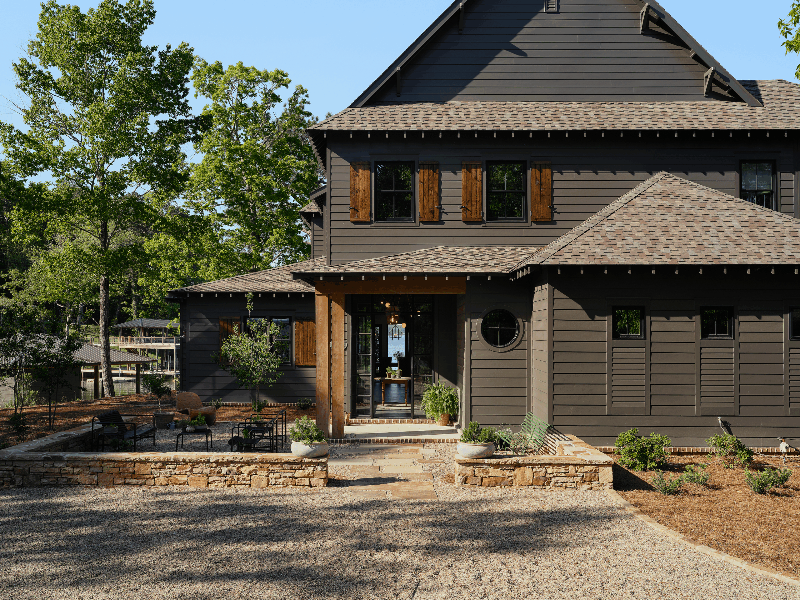 Gravel courtyard entrance at a Lake Martin home with stone retaining walls and board-and-batten siding.