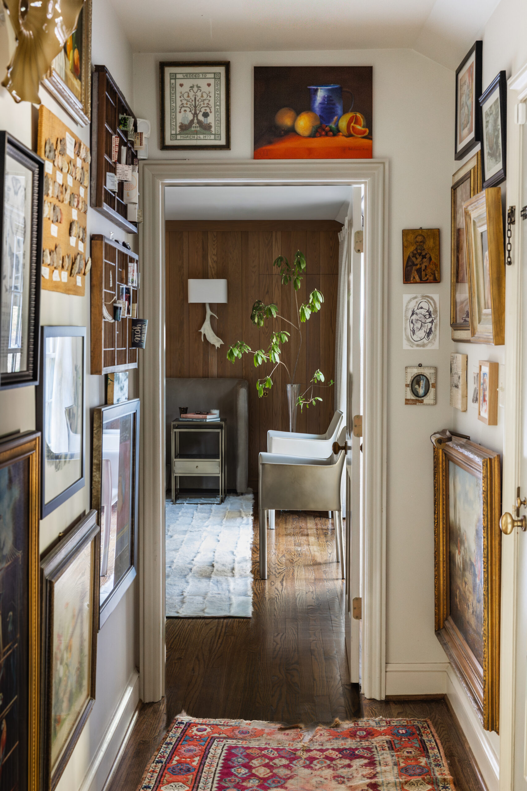 Hallway gallery wall layered with framed art, icons, and vintage shelves in a Mountain Brook home