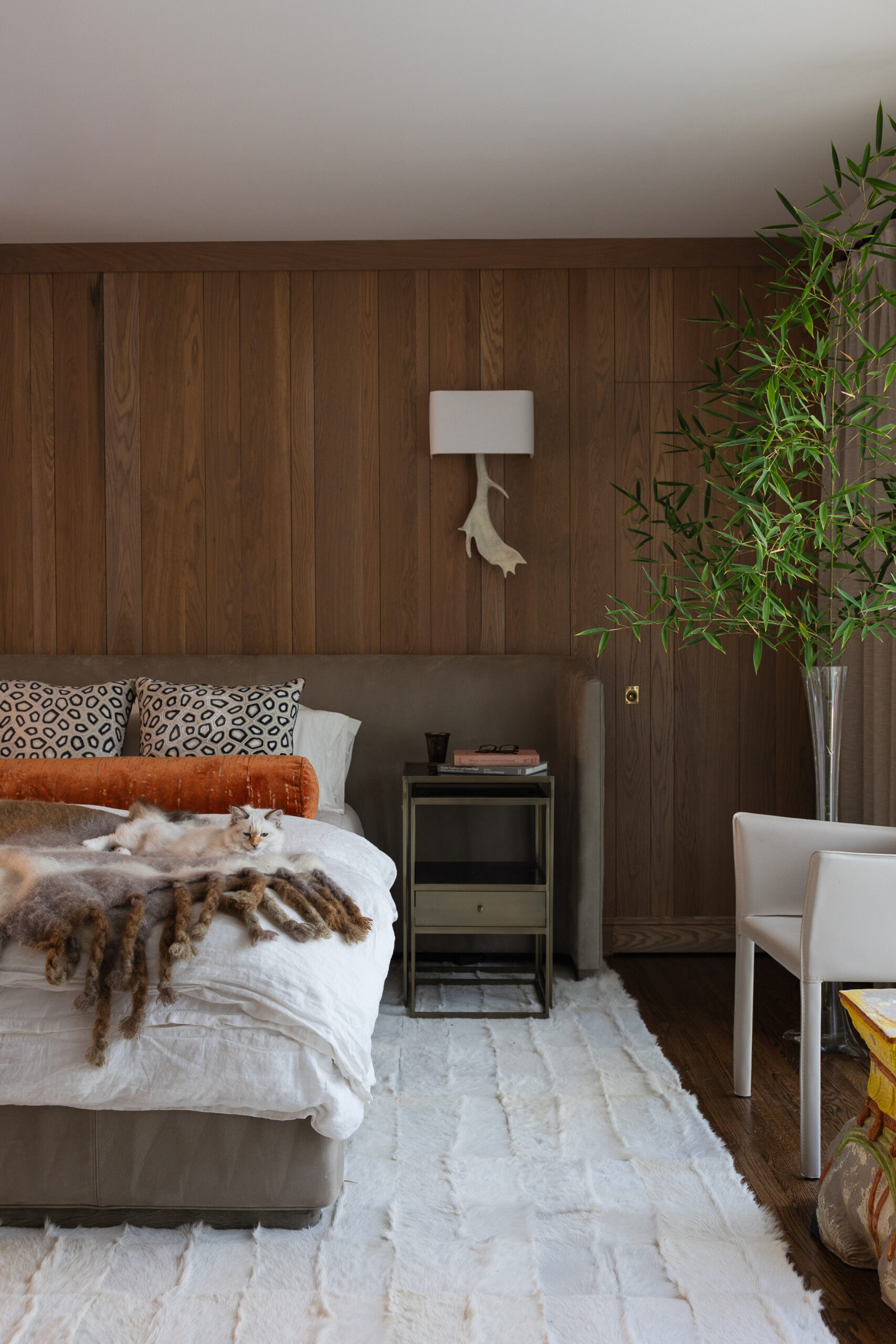 Primary bedroom with a wood-paneled wall, animal print pillows, and a cowhide rug in a Mountain Brook home