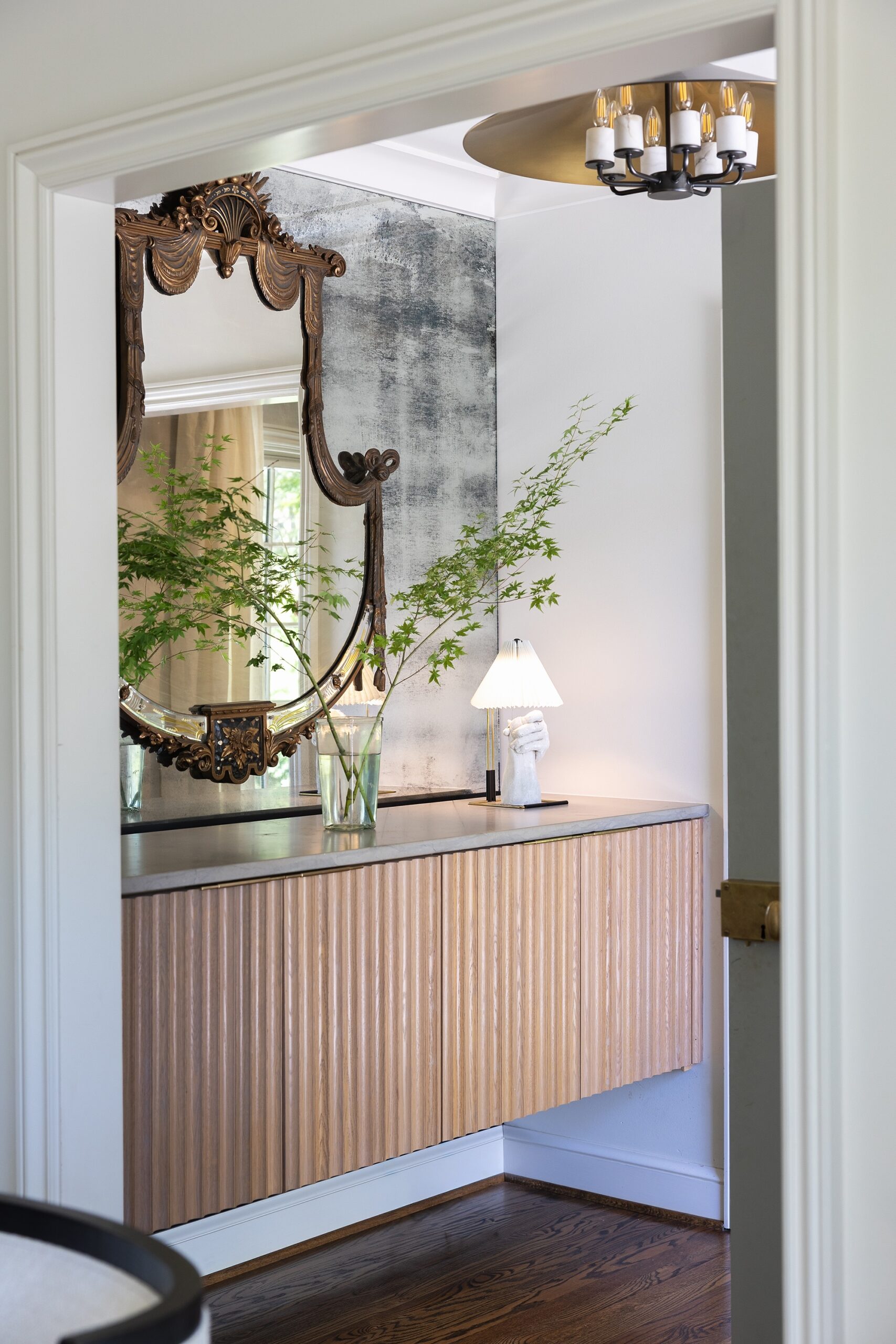 Floating fluted wood console beneath an antique mirrored wall and ornate French mirror in a Mountain Brook home entry