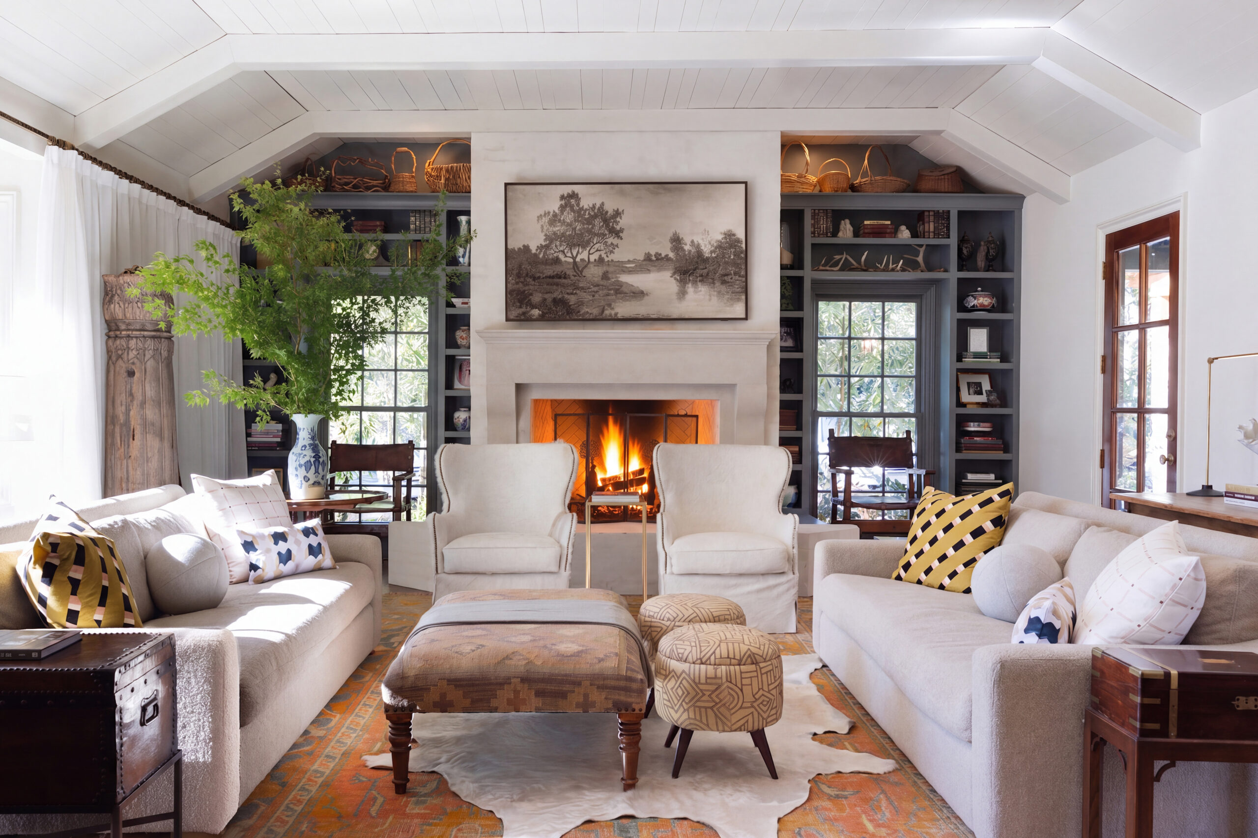 Living room with a fireplace, white wingback chairs, an orange Oushak rug, and gray-green millwork bookcases in Mountain Brook home