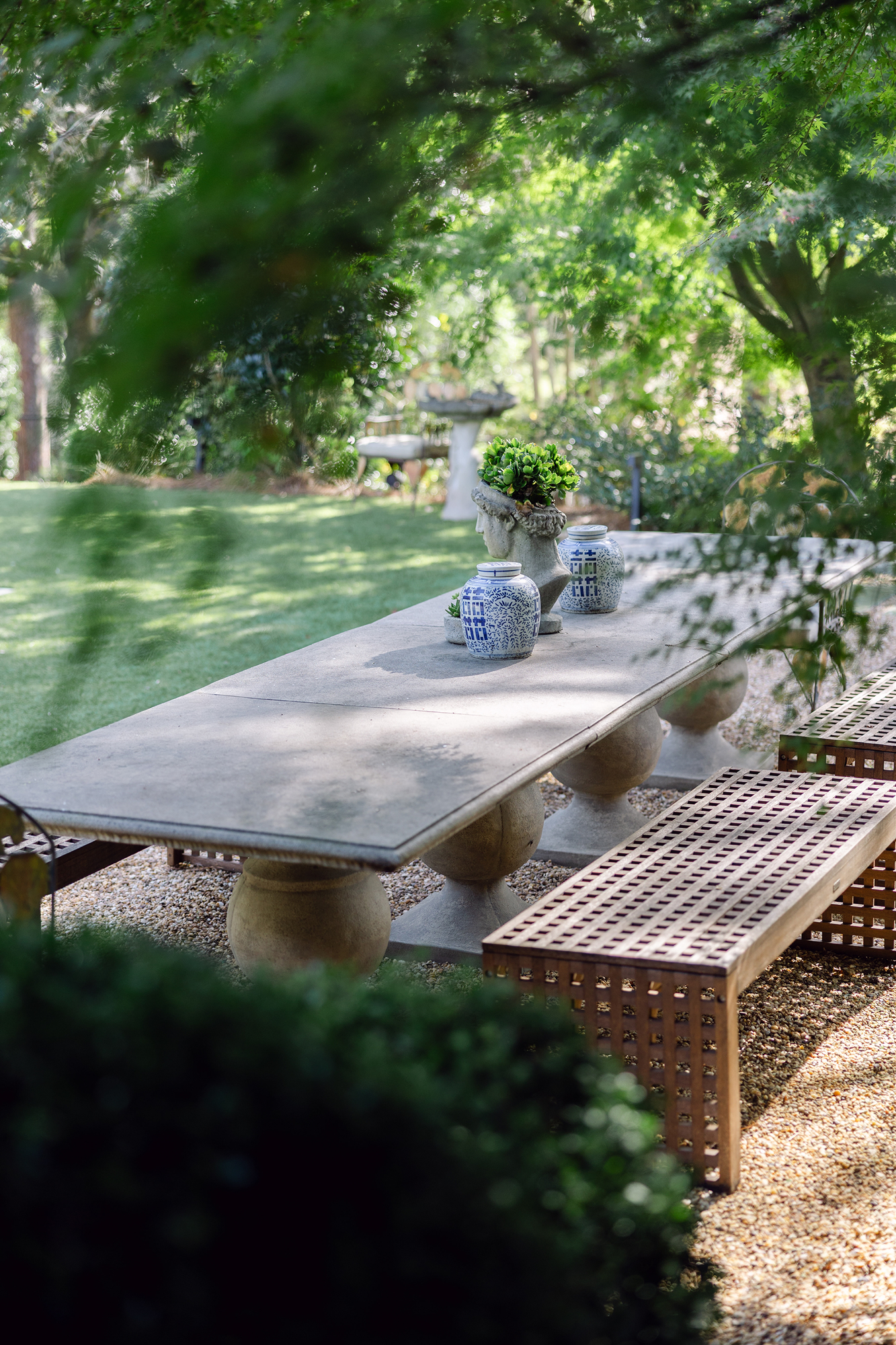 Long wooden outdoor dining table set with place settings and floral centerpieces in a Mountain Brook woodland garden.