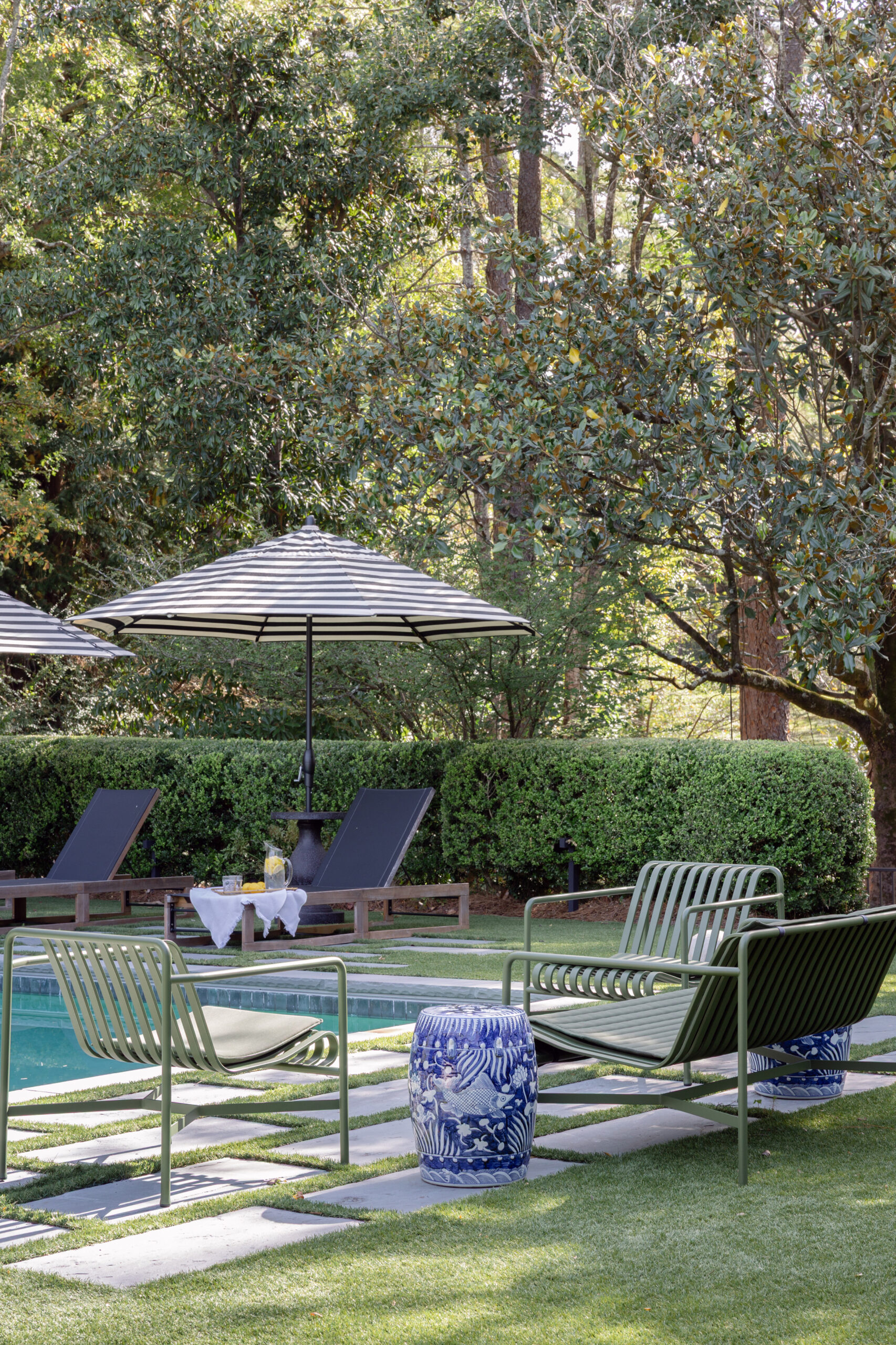 Woodland pool deck with olive-green lounge chairs, a blue-and-white garden stool, and stone pavers set in turf in Mountain Brook home